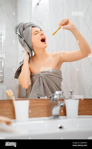 women-after-a-shower-brushes-her-teeth-and-sings-into-a-wooden-toothbrush-2GMFHY0
